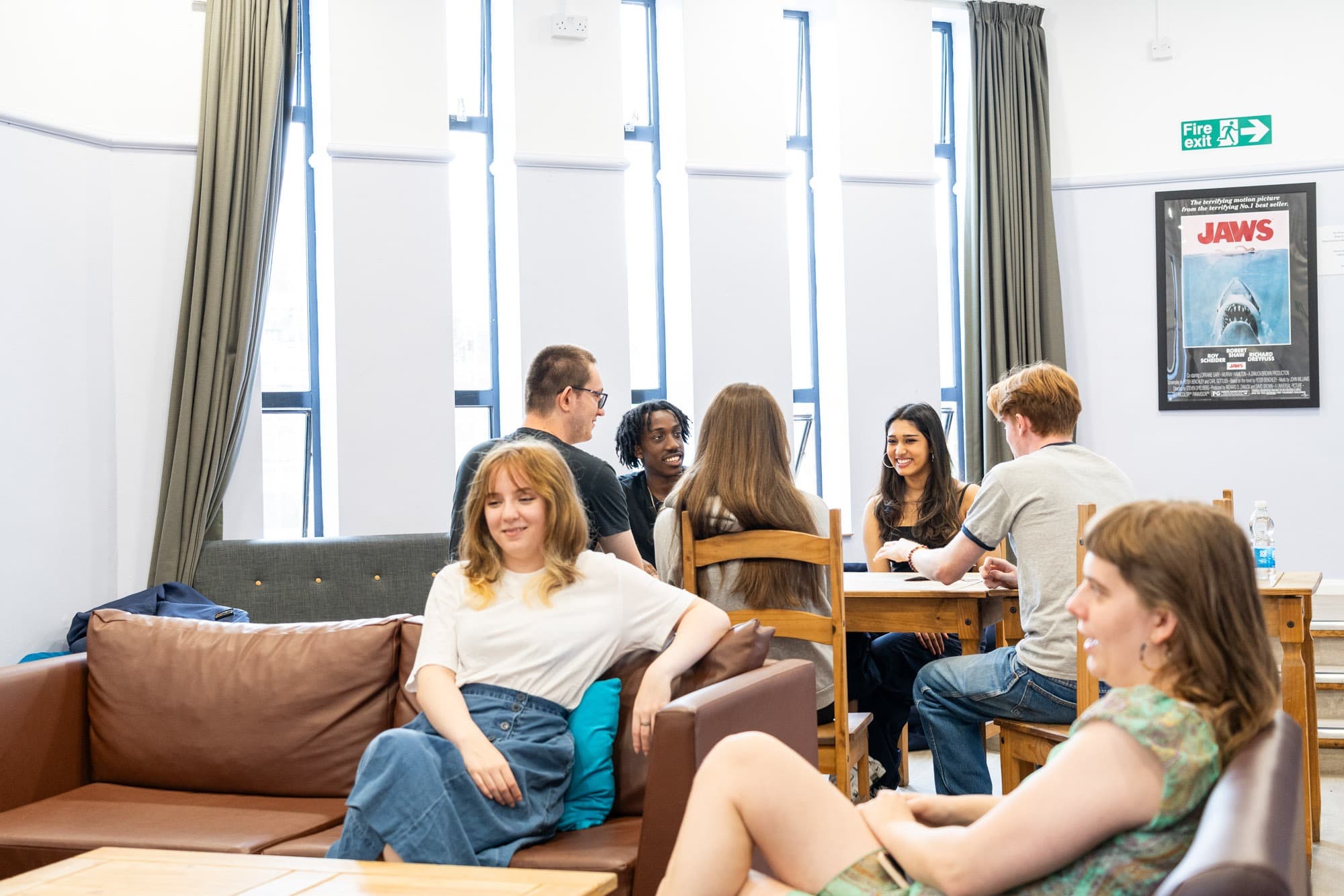 Students chatting on sofas in a common room with tall windows