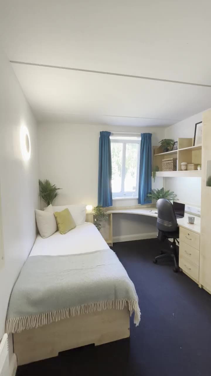 An en-suite bedroom at Broadgate Park: bed, desk and window with blue curtains